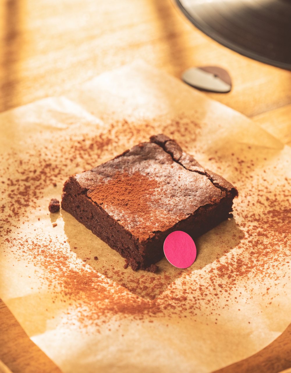 A Melody Bakes brownie dusted with cocoa beside a record and a guitar pick